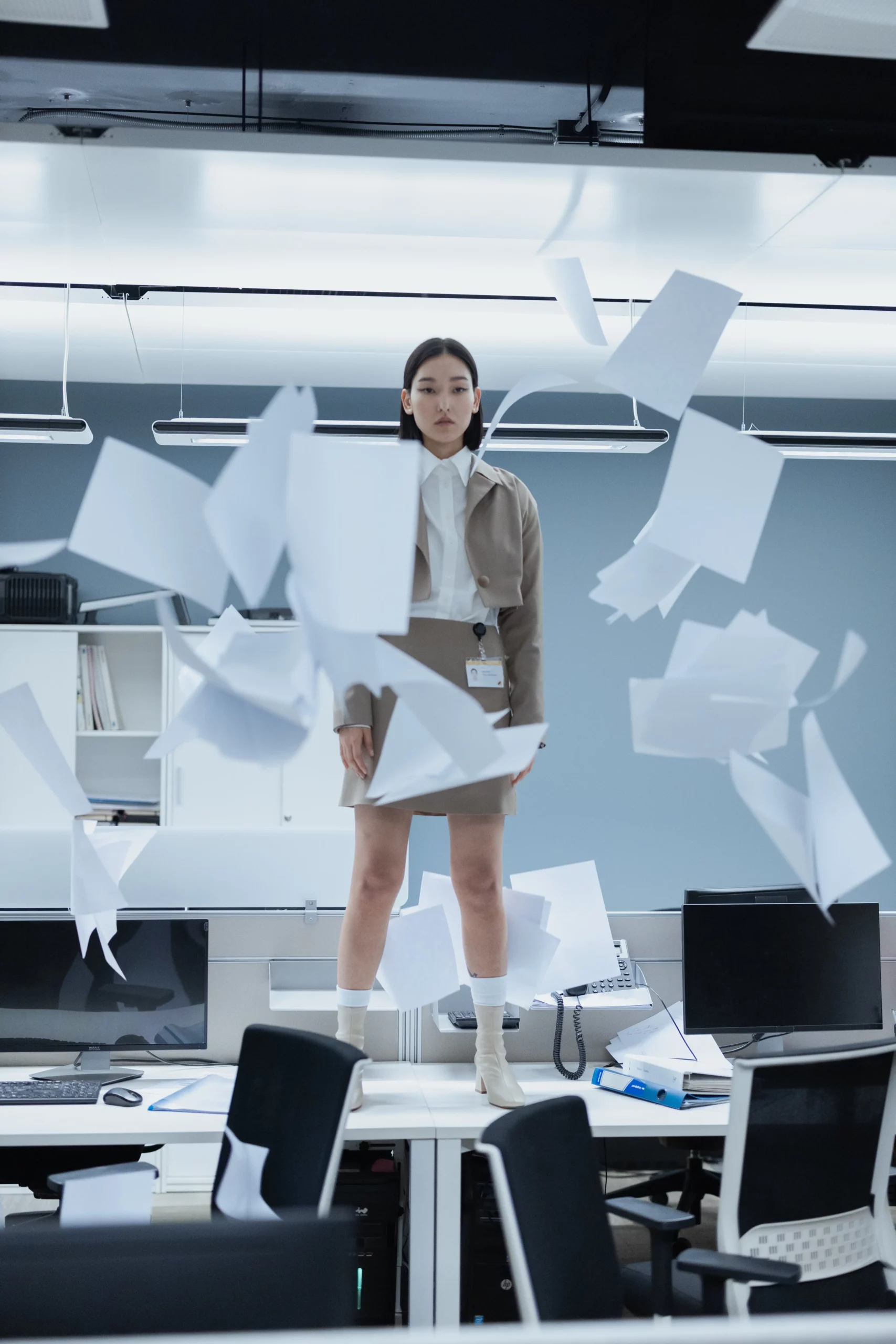 Mujer de pie en oficina con papeles en el aire cayendo haciendo referencia de la no utilización de papel para la documentación