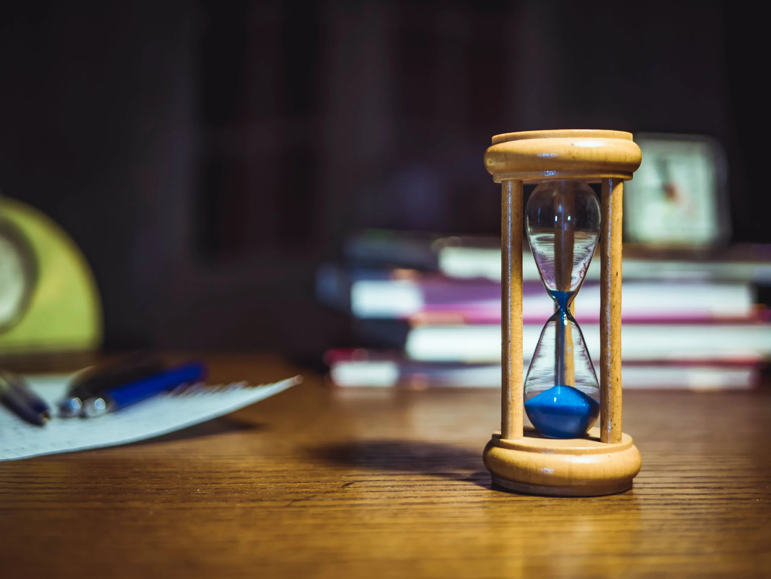 Reloj de arena sobre mesa con libros en el fondo haciendo referencia sobre la gestión del tiempo