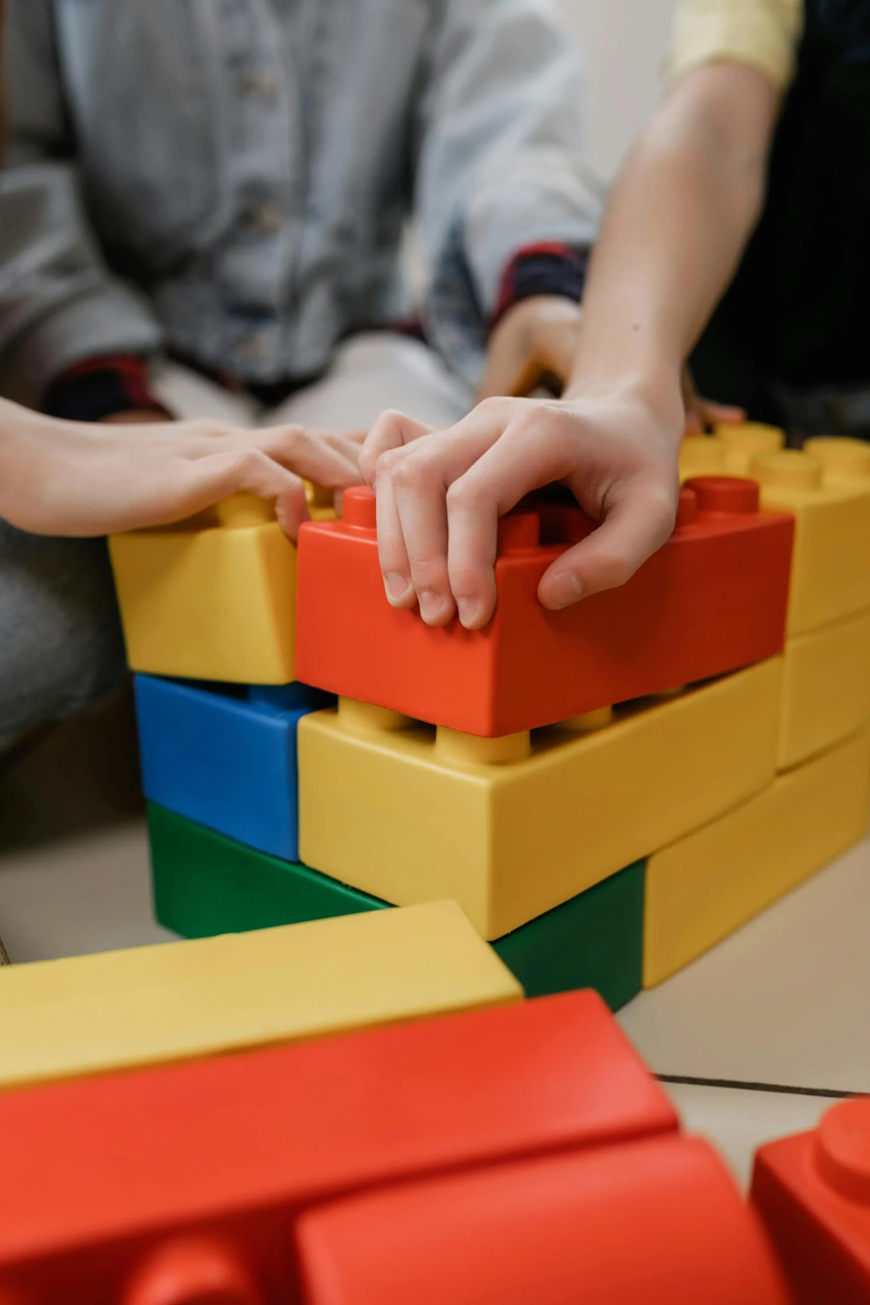 Se muestra en imagen las manos de unos niños apilando bloques de colores