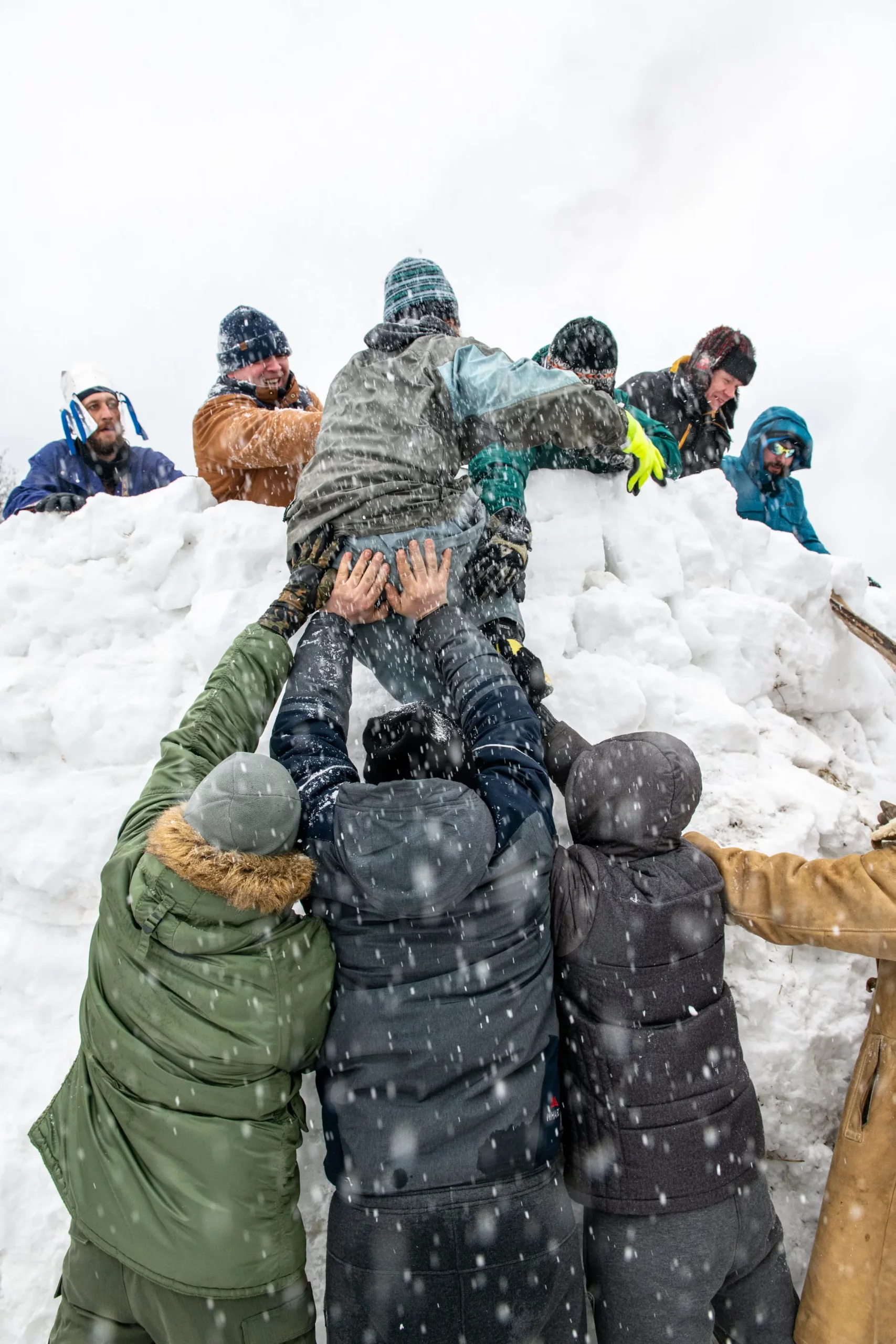 Personas ayudando a un alpinista a subir una montaña de nieve, representando el trabajo en equipo y liderazgo para lograr un objetivo y realizar una tarea con control y calidad.