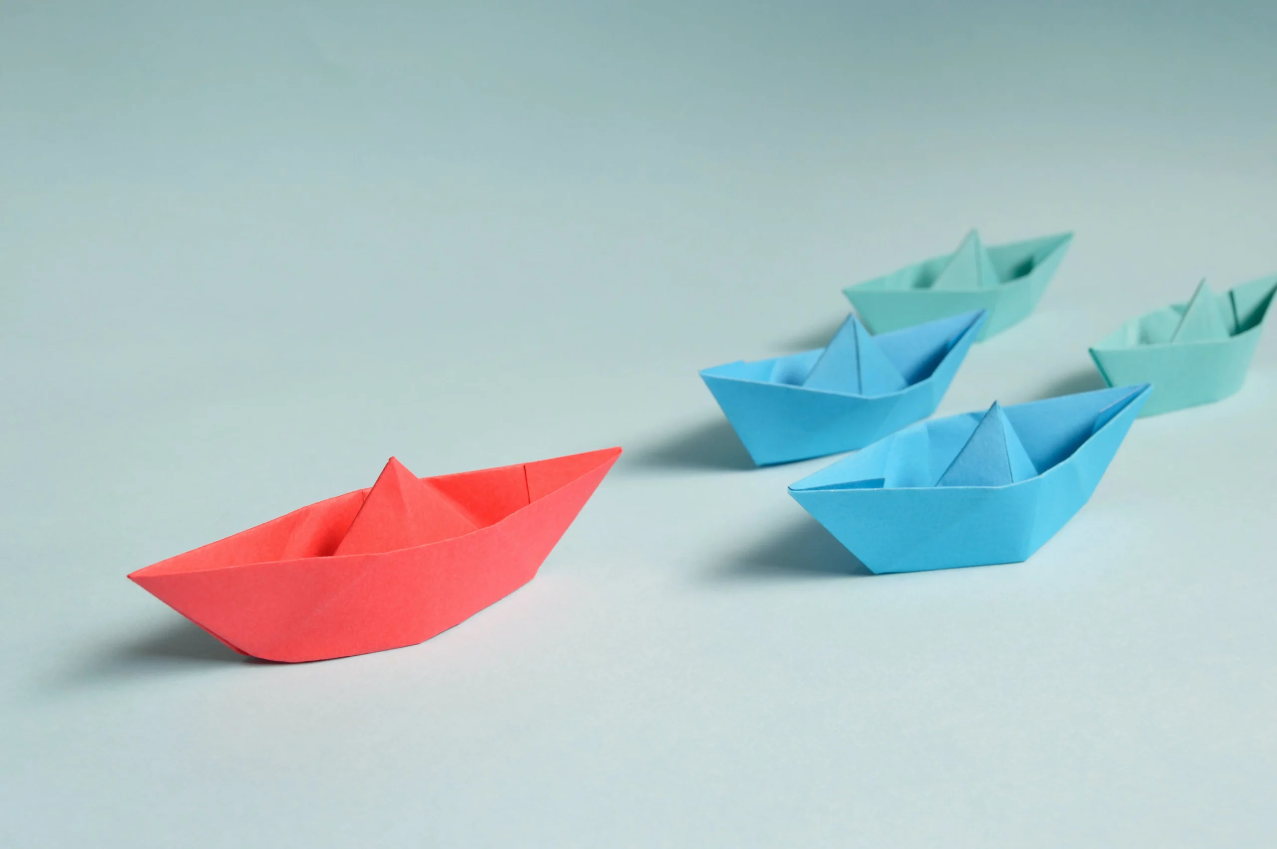 La imagen representa un conjunto de barquitos de papel, siendo liderados por un barco rojo, dirigiéndose para adelante
